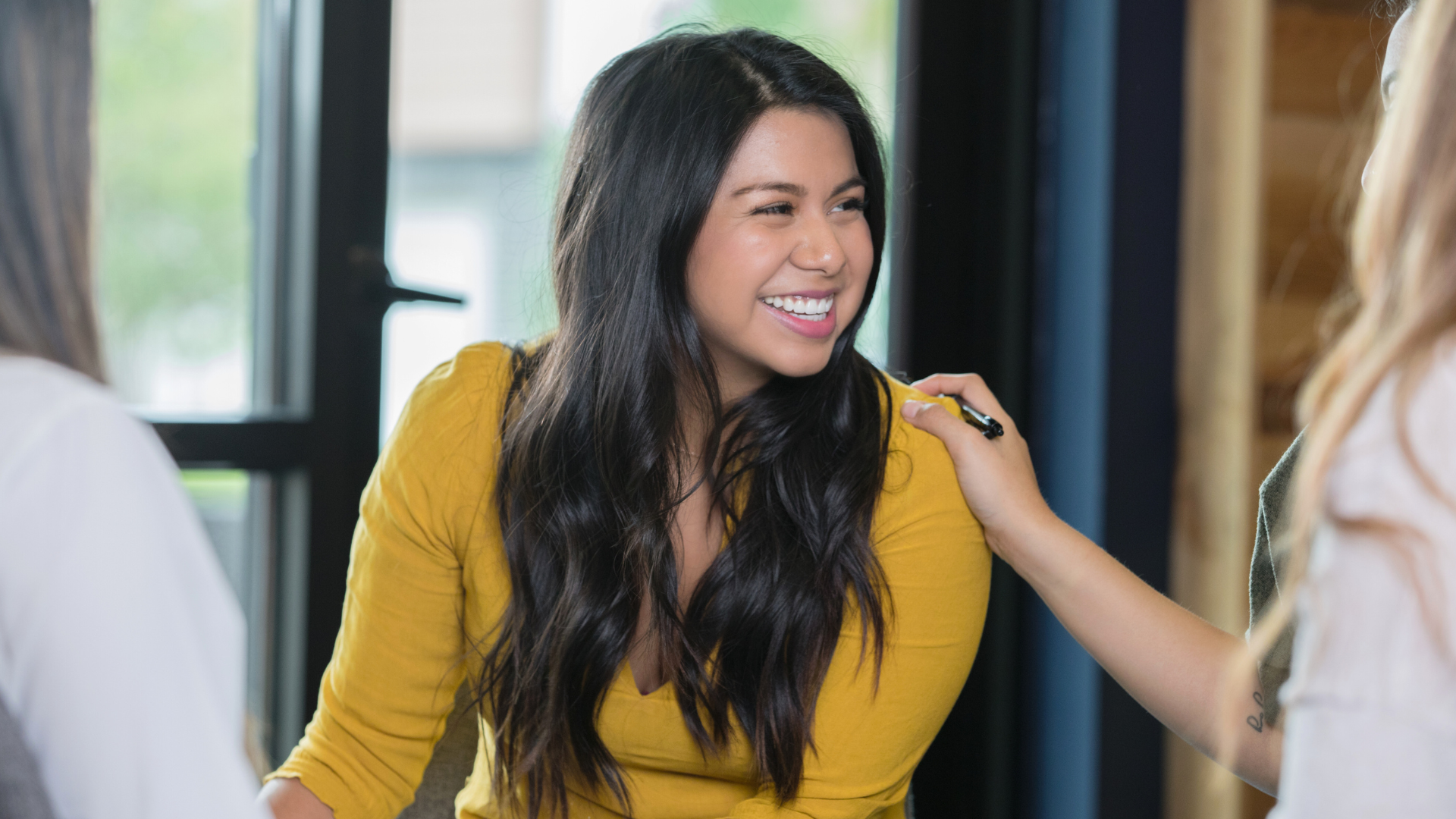 women in mustard top smiling as other women are around her supporting her
