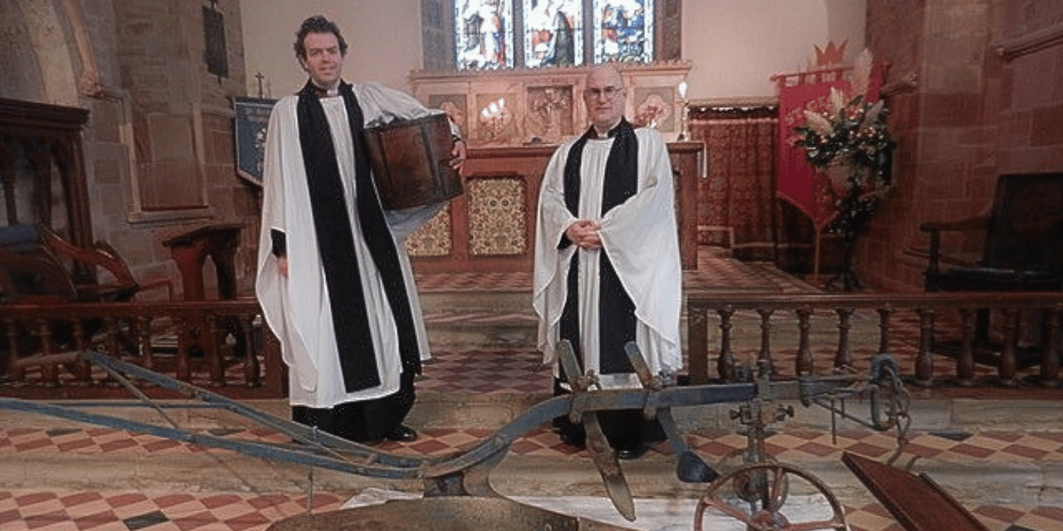 Two vicars stood in front of an ancient plough at the high altar Fownhope Church, Hereford