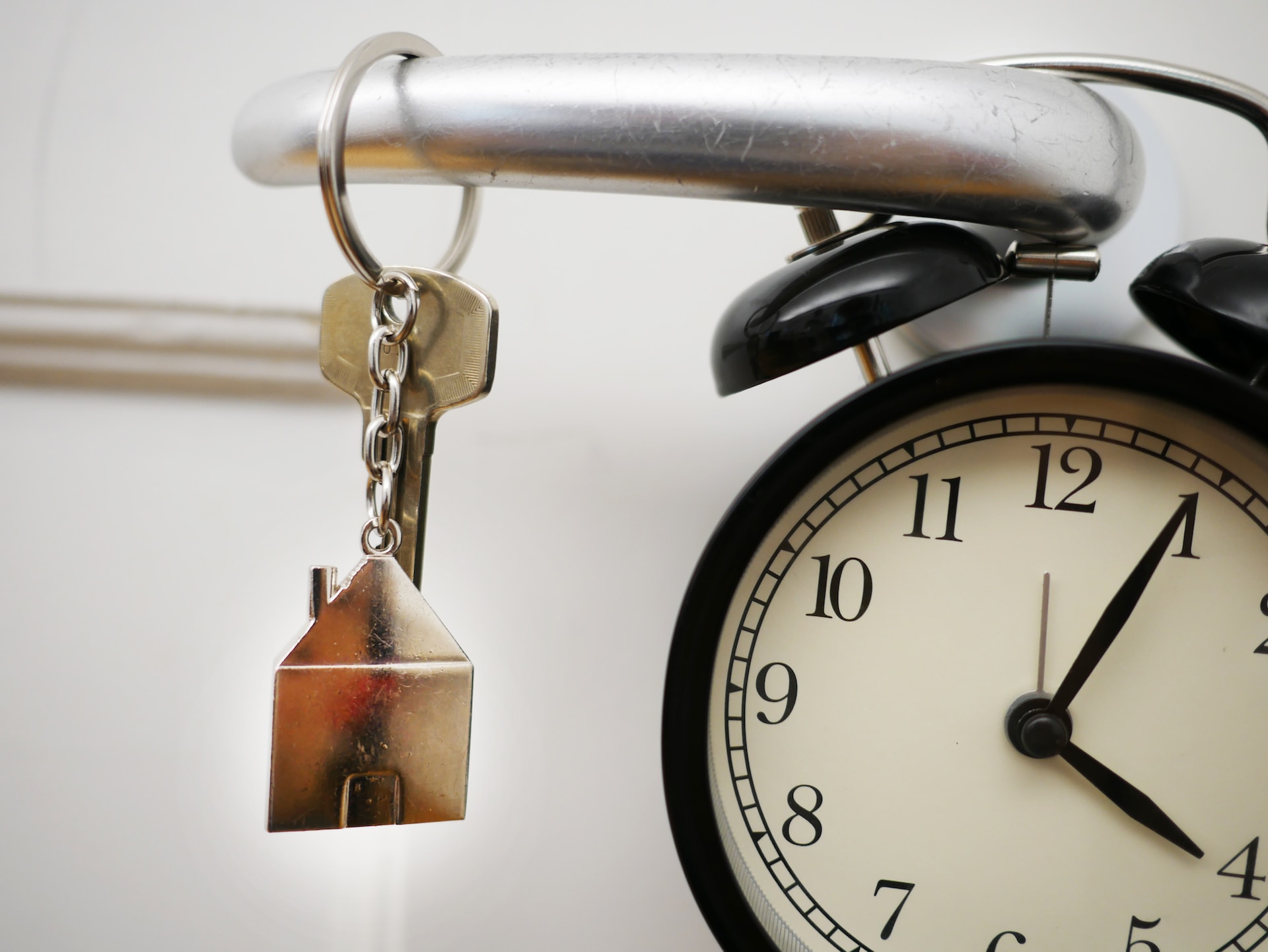 Image of house shaped key ring handing off a bicycle handlebar with a clock in background