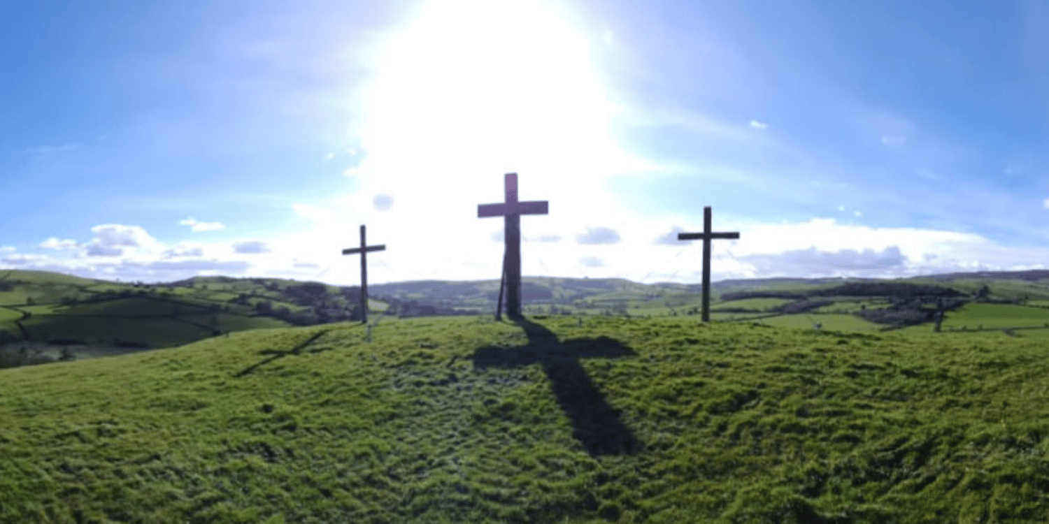 Three wooden easter crosses atop a hill with sunlight and blue sky in background