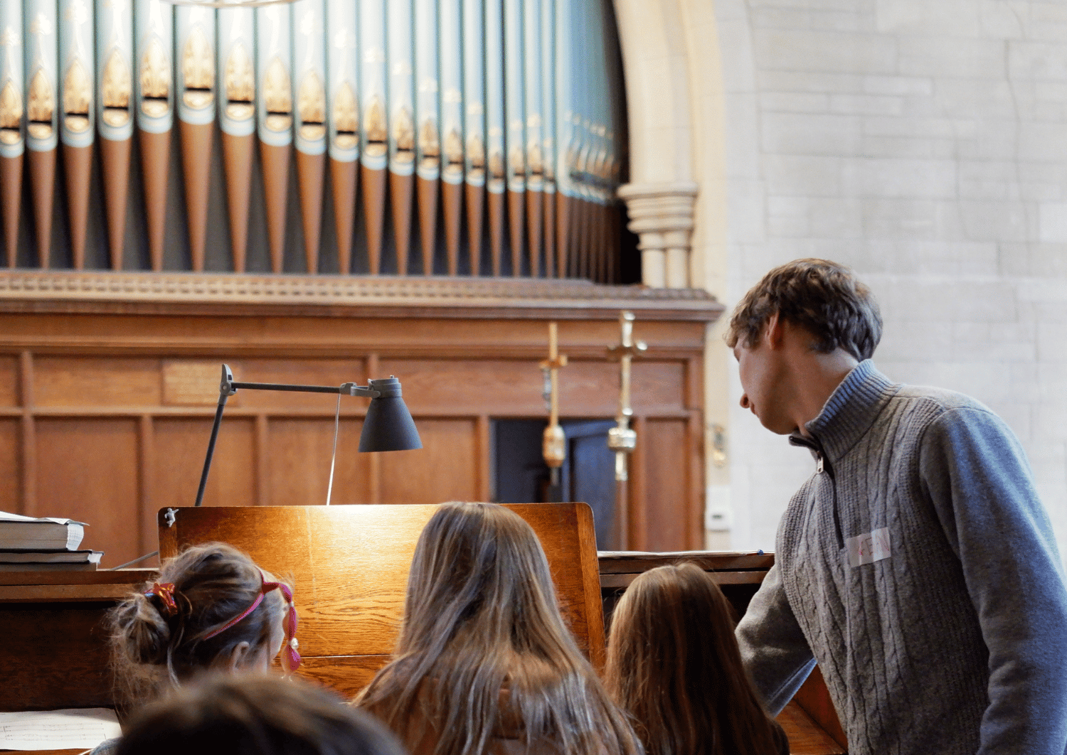 Man stood pointing at music in front of church organ with three girls sat on stool playing organ