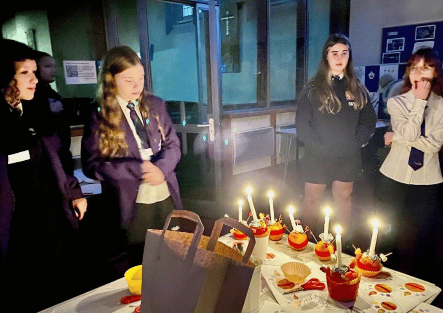 Young people stood inside a church, around a table, illuminated by candles stuck in oranges, decorated with sweets. Celebrating Christingle