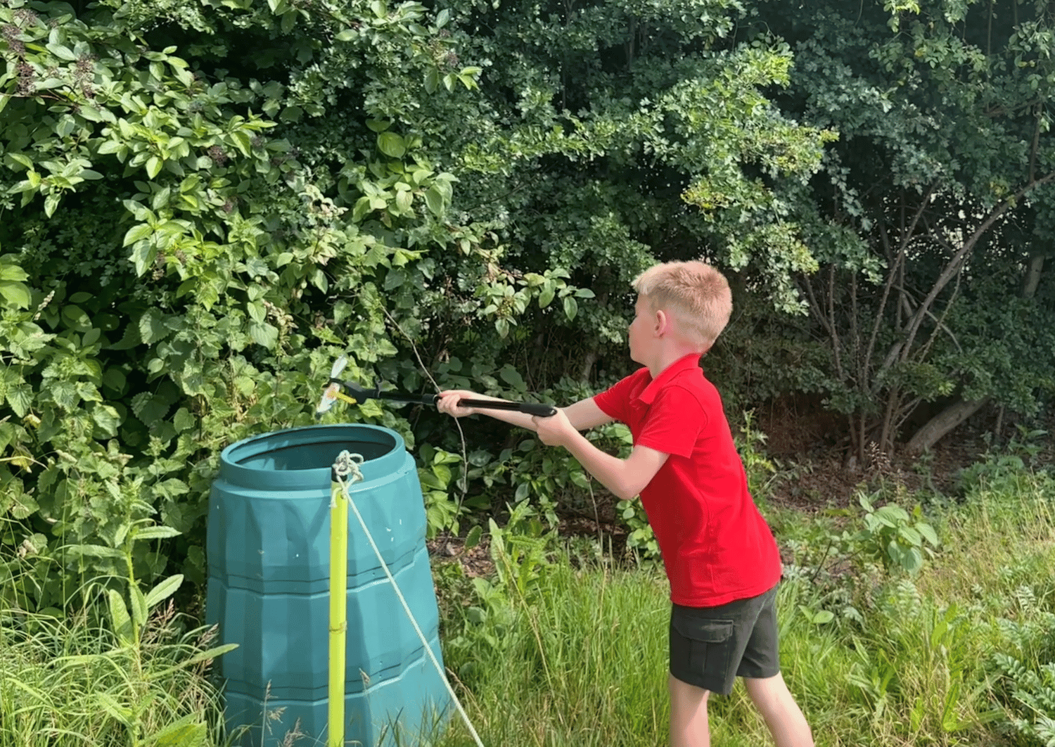 school child wearing red tshirt and grey shorts using a litter picking tool to drop litter into a dustbin