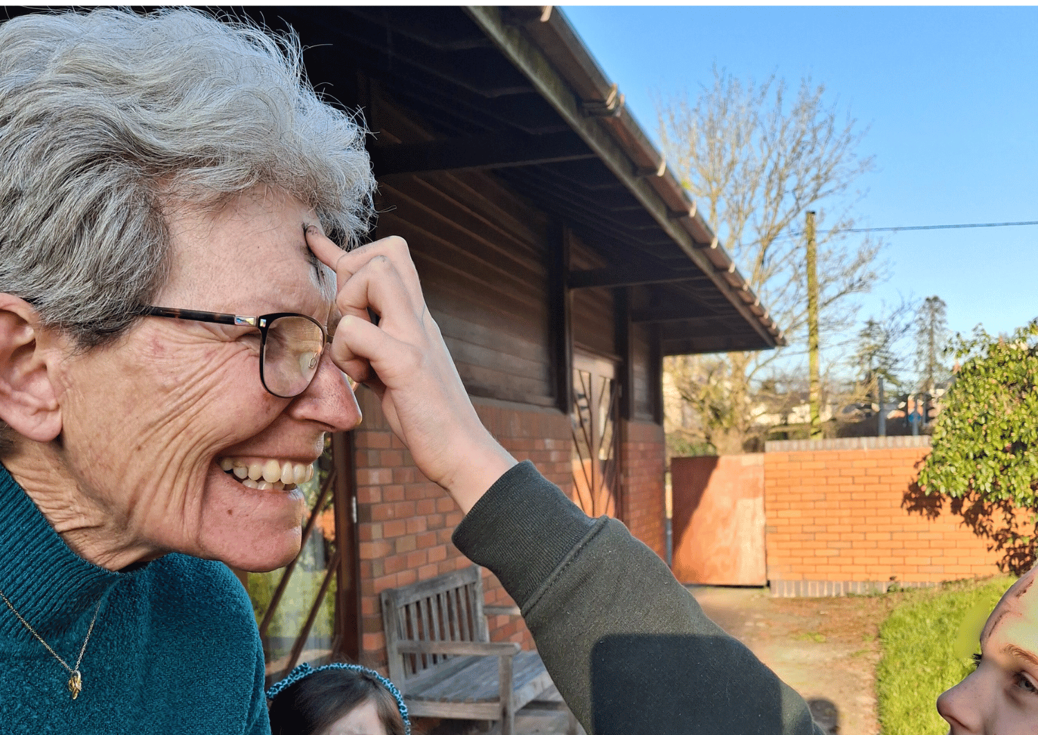 Blue sky and older lady in side profile having ashes marked on her forehead by young person