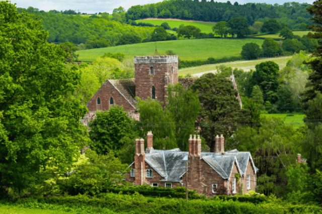 Church with red brick property in front surrounded by trees and hills