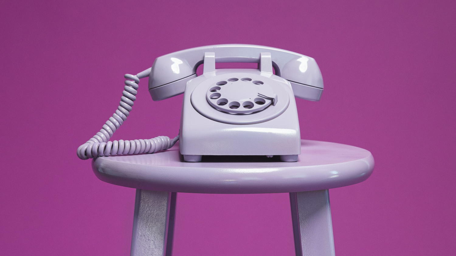 Image of a purple rotary phone on a purple stool against a purple background