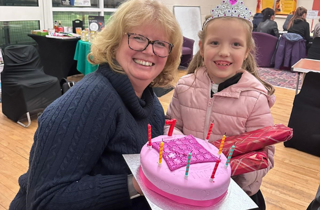 woman bent down next to a girl holding a decorated cake